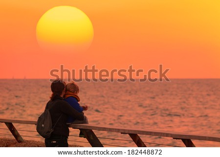 Silhouettes of mother and son on calm ocean sunset background