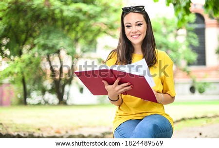 Beautiful female college student reading a book on a bench in a park