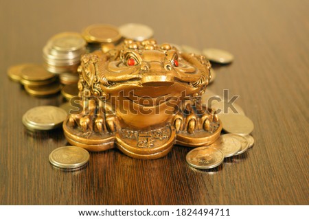 A metal toad next to a stack of coins. Symbol of happiness and financial success.