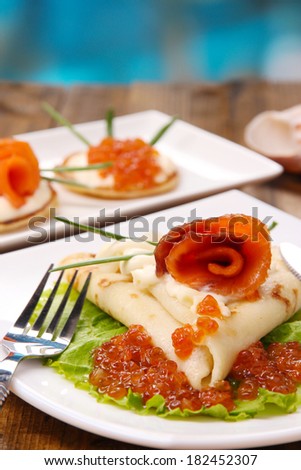Pancakes with red caviar, salmon and mayo, green onion, on plate, on wooden  table, on bright background