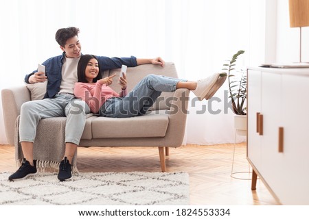 Asian Millennial Couple Using Smartphones Relaxing Sitting On Couch At Home On Weekend. Gadget Lifestyle, Mobile Application, Phone Users Browsing Internet Concept. Empty Space Royalty-Free Stock Photo #1824553334