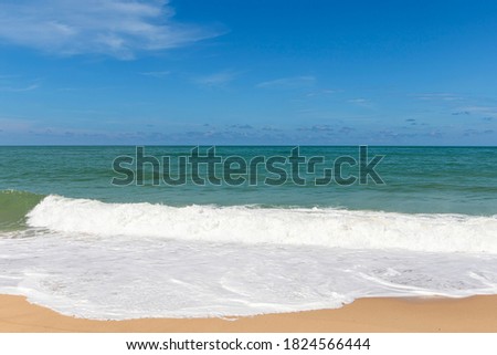 Sandy beach with sea waves and blue sky background.