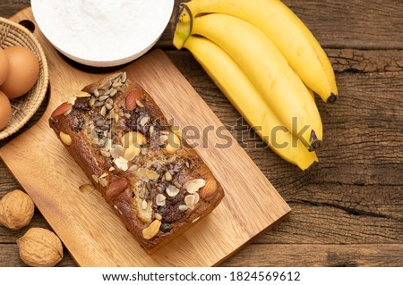 Banana cakes are placed on a wooden tray on a wooden table, with bananas, eggs, flour as background. Top view picture.