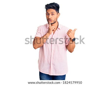 Handsome latin american young man wearing casual summer shirt asking to be quiet with finger on lips pointing with hand to the side. silence and secret concept. 