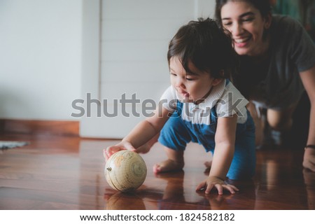 Cheerful young mother playing with excited little boy while spending time together and having fun in light room at home