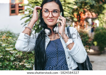 young beautiful stylish woman talking on smartphone, holding backpack, vintage denim style, smiling, happy, summer vaction