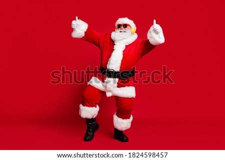 Full body size photo of pensioner old man grey beard show thumbs up party dancing wear santa x-mas costume coat sunglass headwear wireless earphones boots isolated red color background