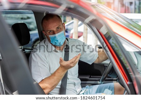 Handsome businessman,looking at camera,wearing protective face mask while sitting in a car.