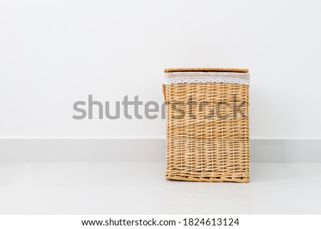 Rattan basket for clothes storage with white wall background inside bedroom.