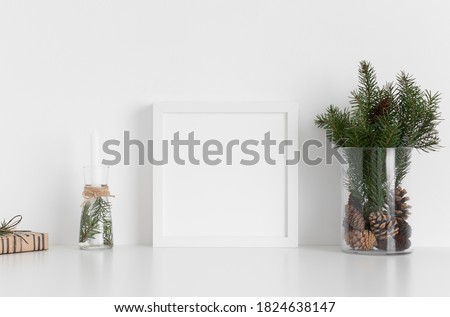 White square frame mockup with a bouquet of fir, candle and a gift on a white table. Christmas decoration.