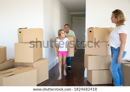 Girl helping parents to move into new apartment. Dad and daughter carrying big cartoon box together. Front view. Moving or relocation concept