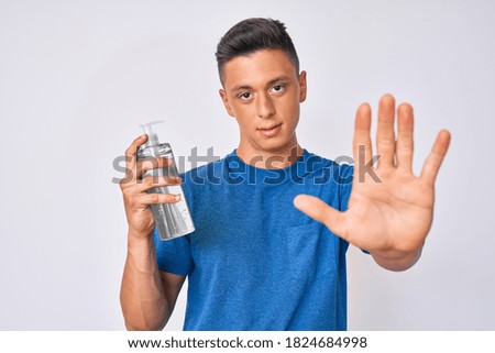 Young hispanic boy using hand sanitizer gel with open hand doing stop sign with serious and confident expression, defense gesture 