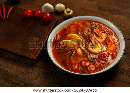 Tom yam soup with shrimp and lime in a light plate on the table ginger, lime and mushrooms.