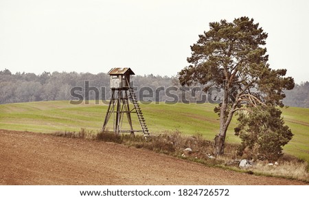 Retro stylized picture of a wooden deer hunting pulpit on a field in autumn.