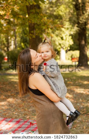 Cute attractive photo of a young woman hugging her baby. Beautiful mother kisses her daughter. Little girl eating lollipop. Yellow leaves, autumn.