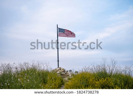 An American flag on the flagpole waving in the wind against clouds sky