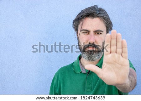 gesture of defense, man in front of a blue wall with open hand making stop sign with serious and confident expression, 