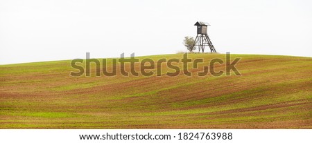 Rural landscape with wooden hunting blind on a field in an autumnal misty morning.