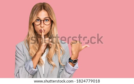 Beautiful blonde young woman wearing business clothes asking to be quiet with finger on lips pointing with hand to the side. silence and secret concept. 