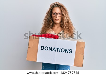 Beautiful caucasian teenager girl volunteer holding donations box relaxed with serious expression on face. simple and natural looking at the camera. 