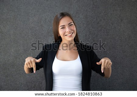 Smiling woman pointing her fingers at something at the bottom of an image, a product, or a blank copyspace for an advertising slogan or text message on a gray background.