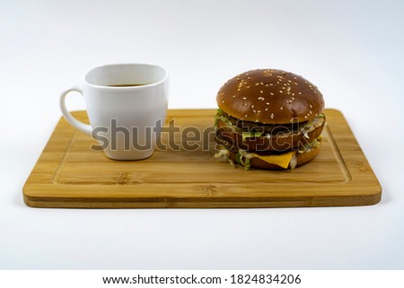 Burger and a cup of black coffee on a cutting board.