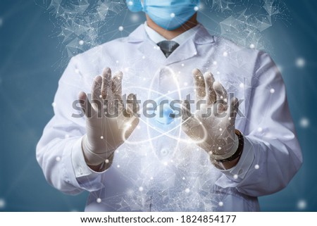 Doctor in a mask on makes manipulations with an atom on a blurred background.