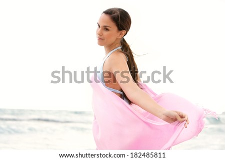 Close up side portrait of a beautiful young woman relaxing on a beach on holiday holding a pink fabric sarong around her body and floating in the breeze, breathing fresh air, lifestyle.
