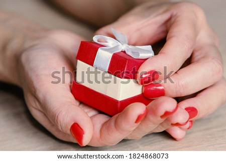 Red gift box of a woman's hands in a beautiful style on a light background. Great design for gift purposes. The concept of the celebration.