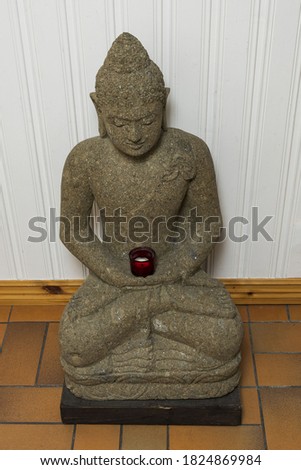 Close up view of grey buddah figure on white wall background. 