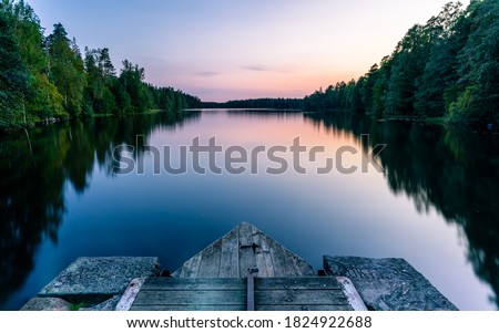 A calm and silent evening at sunset at a small forest lake in Sweden. In the foreground there is a wooden bridge. The lake is surrounded by trees that are reflected in the water Royalty-Free Stock Photo #1824922688