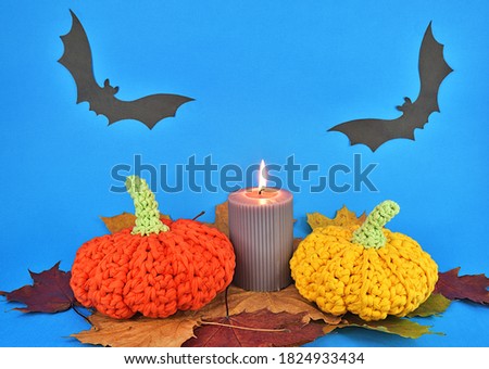 Collage created for Halloween. Knitted pumpkins, burning candle, fallen autumn leaves and two bats on the background.