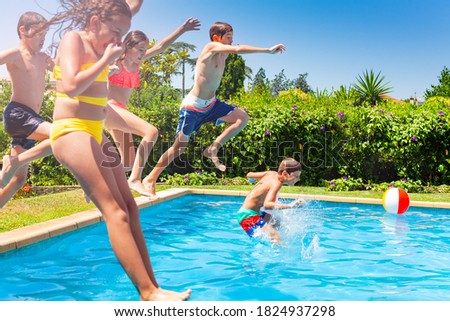 Boys and girls in a group jump in water pool outside during summer vacation