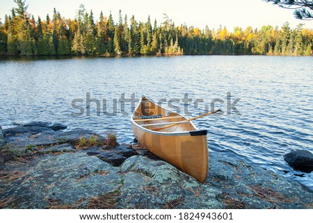 Yellow canoe with paddle on rocky shore of northern Minnesota lake at sunrise during autumn