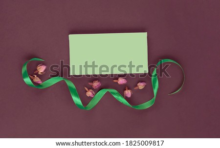 Still life of green ribbon, dry rosebuds and cards for the text.