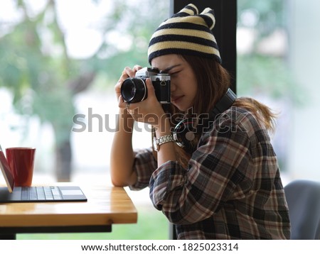 Portrait of female photographer taking photo with digital camera while sitting in cafe