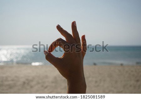 a beautiful female hand demonstrates the symbol OK okay against the background of the sea, clear sky and sandy beach on a clear sunny day
