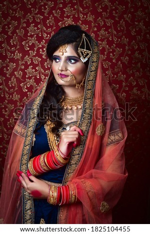 Portrait of an Indian Muslim bride wearing red sari with heavy jewelry in a banquet hall. Traditional Muslim Bride in wedding. Royalty-Free Stock Photo #1825104455