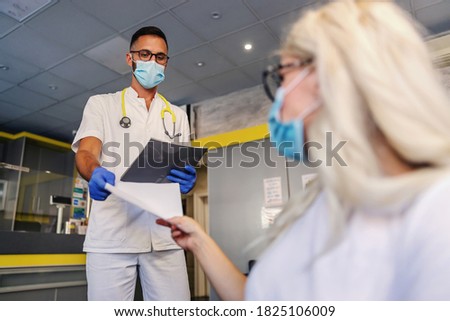 Young medical worker with rubber gloves, face mask, in sterile uniform giving to a female blond patient test results. She is covid negative.