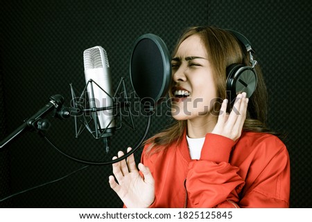 Young pretty woman happy and motivated, singing a song with a microphone in the studio. Enjoy in the moment and freedom.