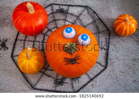 Halloween holiday, carnival background, orange pumpkin with toy scary eyes on a black web and little spiders around.
