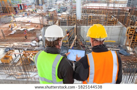 engineer architect with hard hat and safety vest working together in team on major construction site on computer tablet