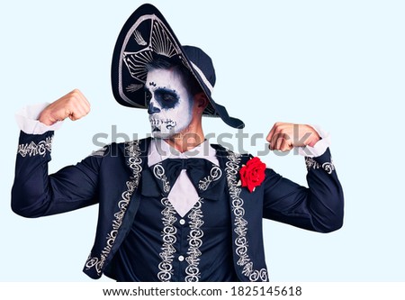 Young man wearing day of the dead costume over background showing arms muscles smiling proud. fitness concept. 