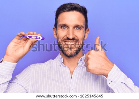 Young handsome man controlling temperature holding thermometer over purple background smiling happy and positive, thumb up doing excellent and approval sign