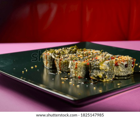 Sushi set served on a black square plate over bright pink background. Traditional Japanese cuisine, sushi rolls close up. Delicious meal.