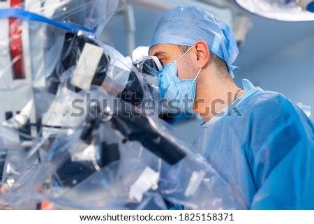 Neurosurgeon with microscope. Doctor in medical mask and scrubs is performing an operation with modern equipment.