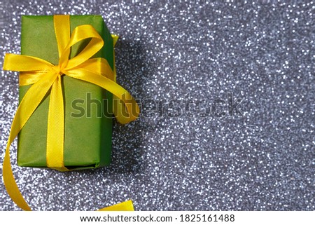 Green box with golden ribbon on sparkling glitter paper backgound. Holiday background. Christmas concept.