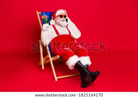 Portrait of his he nice handsome bearded fat Santa hipster sitting in chair drinking cocktail calling abroad home roaming cellular contact isolated bright vivid shine vibrant red color background