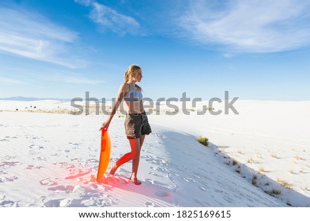 Teenage girl with a sledge at the top of a rise at White Sands Nat'l Monument, NM