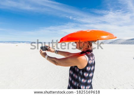 woman carrying orange sled on her head,taking selfie,White Sands Nat'l Monument, NM